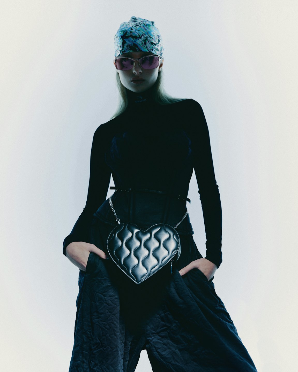 Woman wearing a headscarf and pink sunglasses poses with a heart-shaped bag.