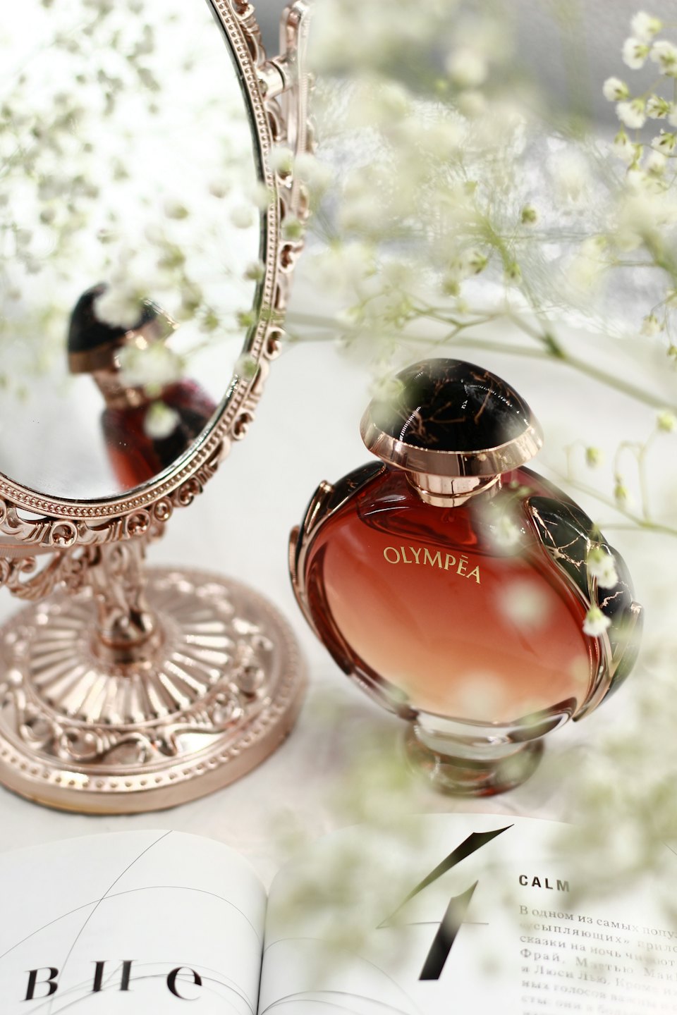 Ornate rose gold vanity mirror reflecting a perfume bottle on magazines.