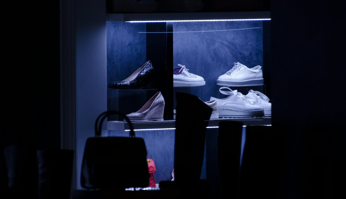 Luxury shoes and handbags displayed on illuminated store shelves.
