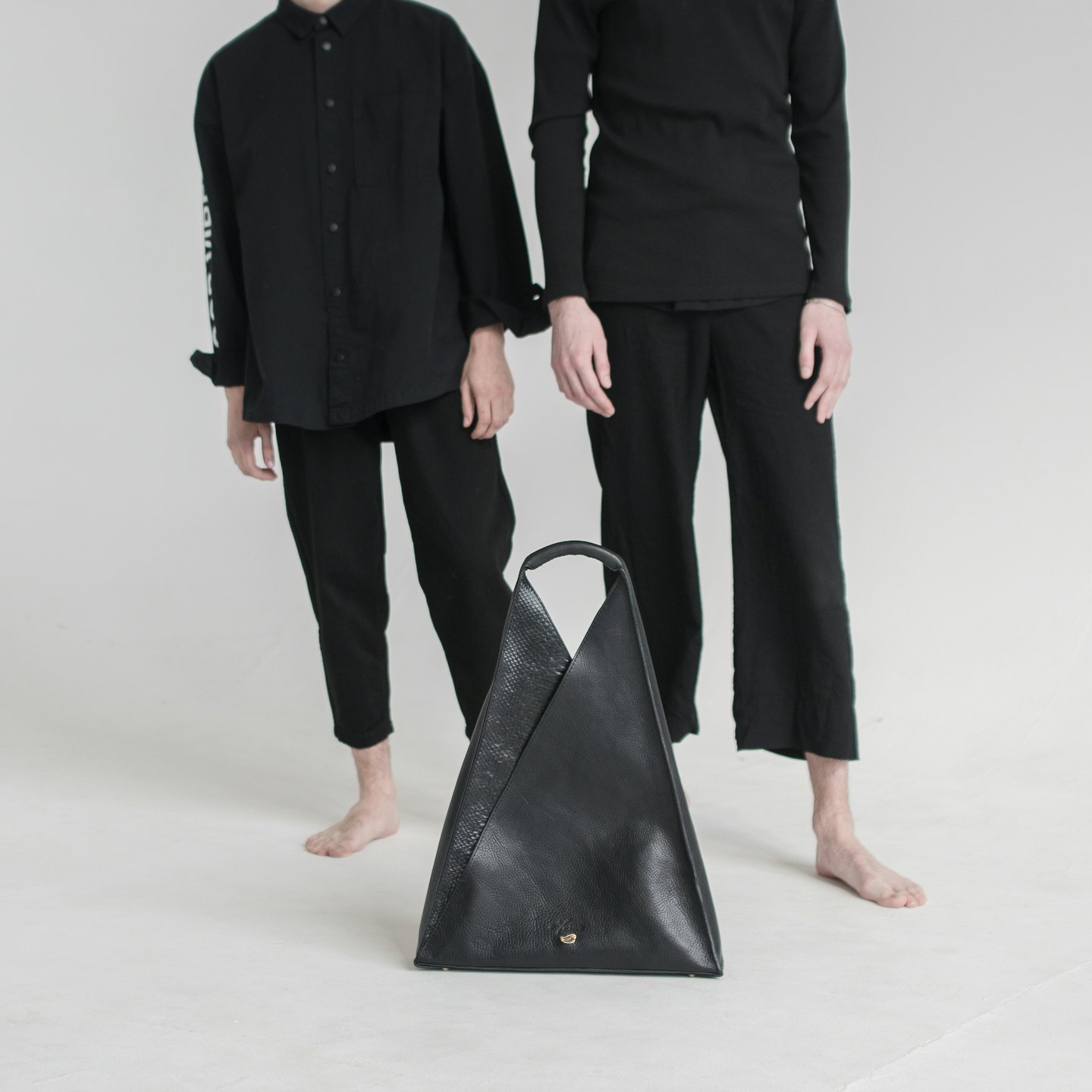 A black leather triangular handbag rests on the floor.